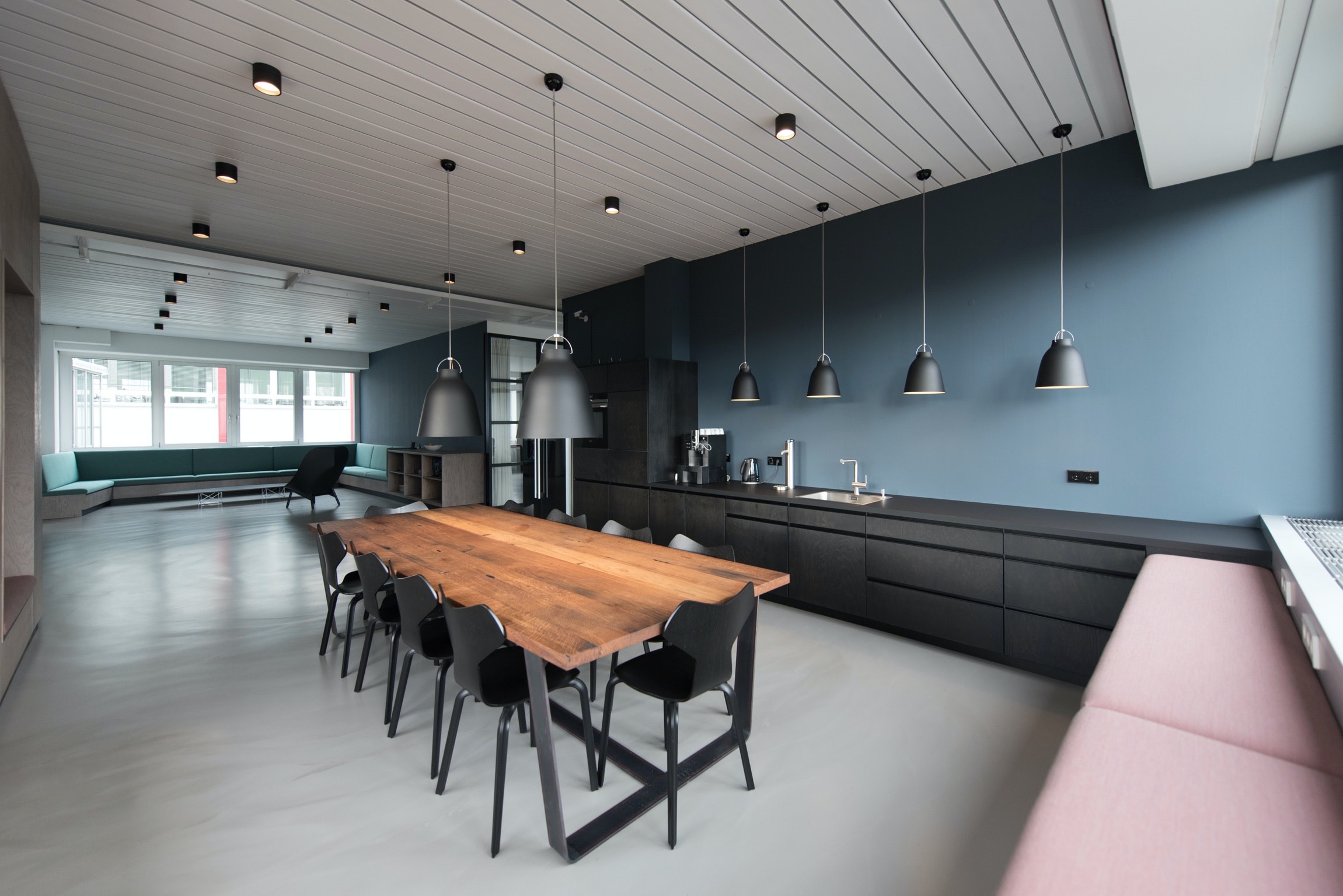 Modern kitchen with a long wooden table, black chairs, and pendant lights.